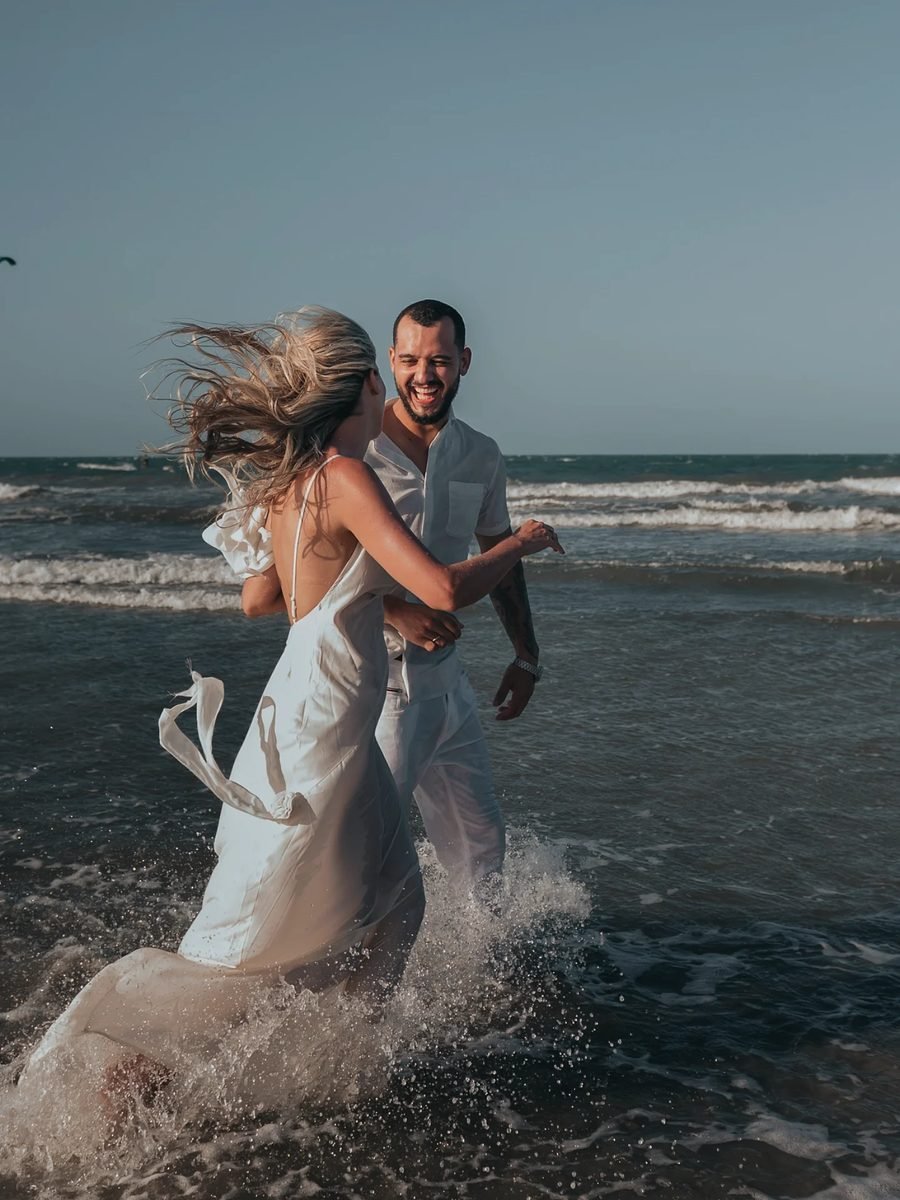 Ensaio de casal na praia, vestidos de branco entre as ondas